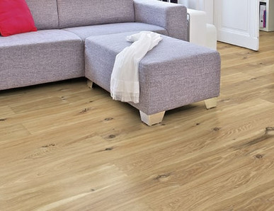 Im Wohnzimmer ist Parkett in Langdielen-Optik verlegt. Dazu passt ein Ecksofa mit bunten Kissen.