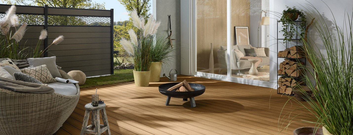Helle Terrasse vor einem Haus, umgeben von einem Sichtschutzzaun mit dekorativen Elementen.